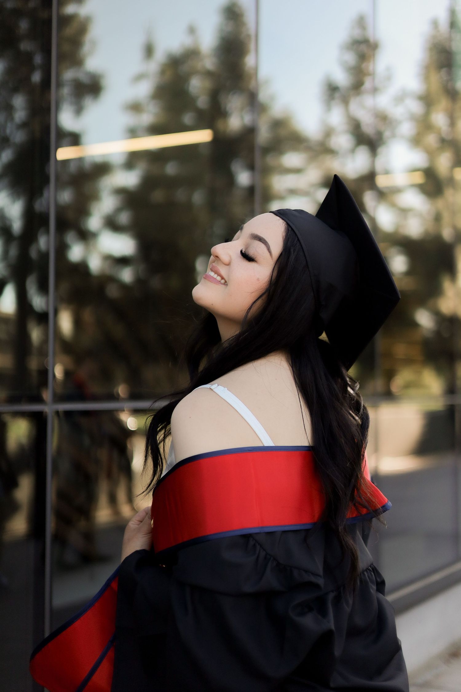 A graduation photoshoot featuring someone in academic regalia with a black cap and red sash.