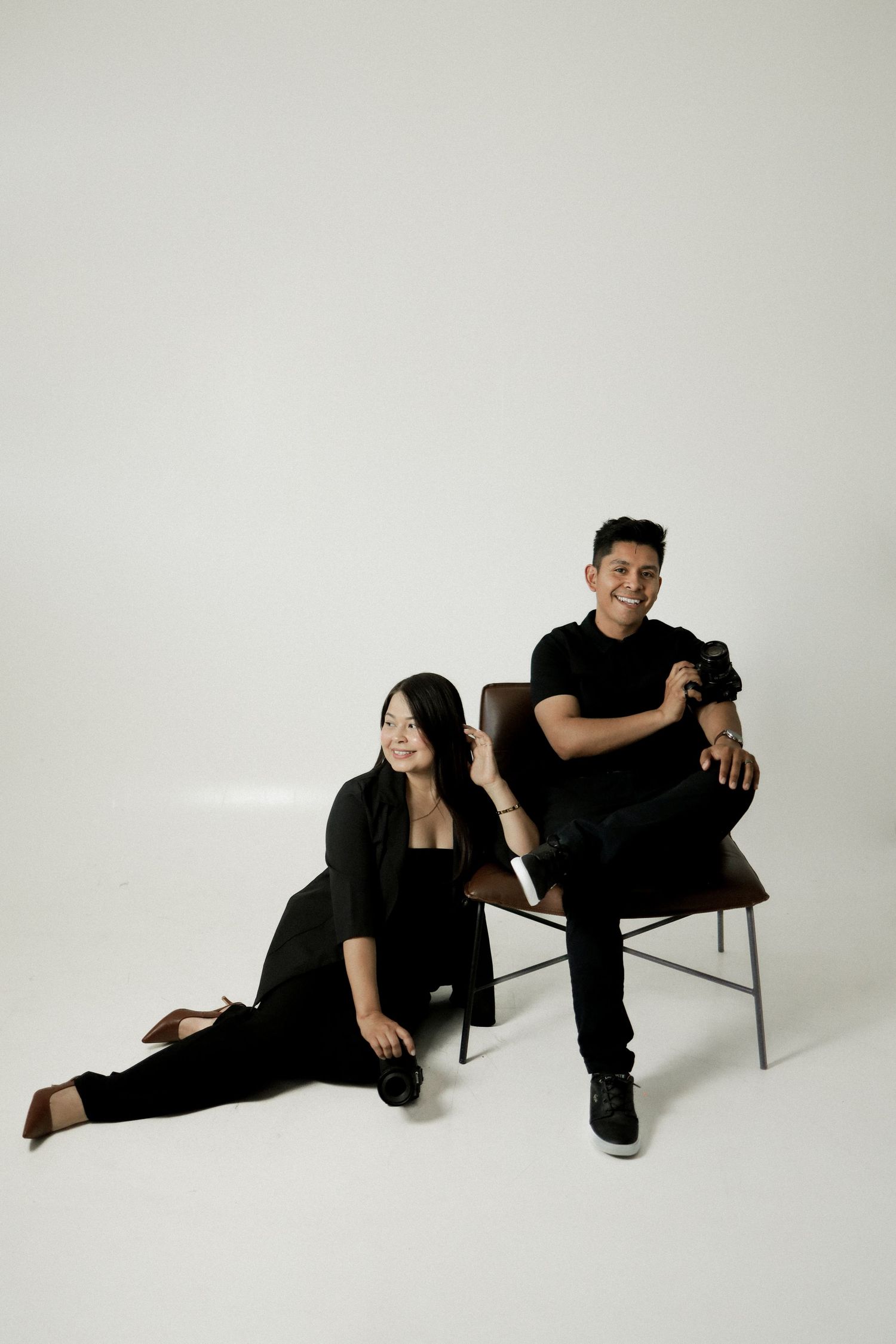 Minimalist studio photoshoot with couple in black clothing posing on chairs.