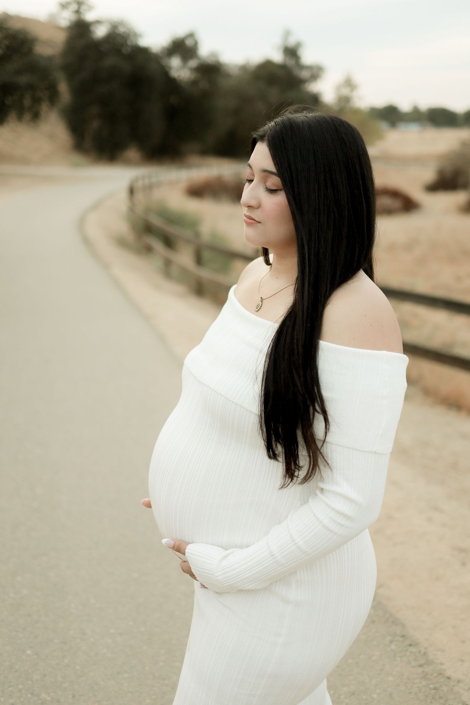 Maternity photoshoot featuring an off-shoulder white sweater against a desert landscape.