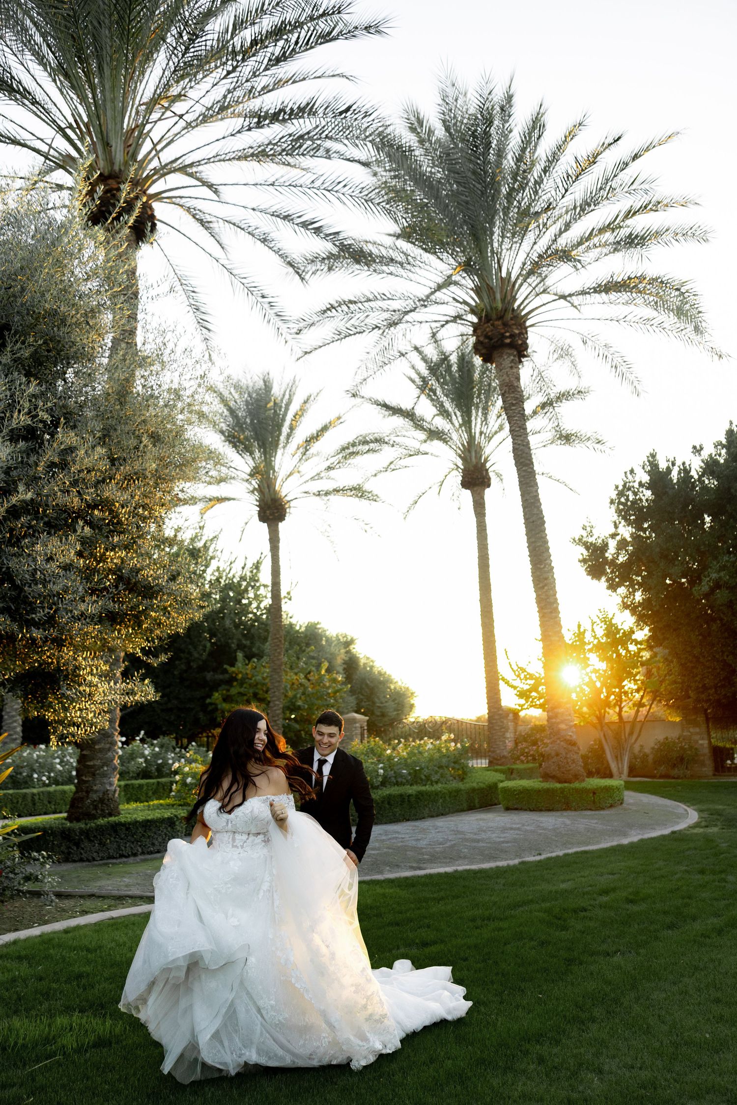Newlyweds pose in a garden with tall palm trees and sunset lighting creating a romantic atmosphere.