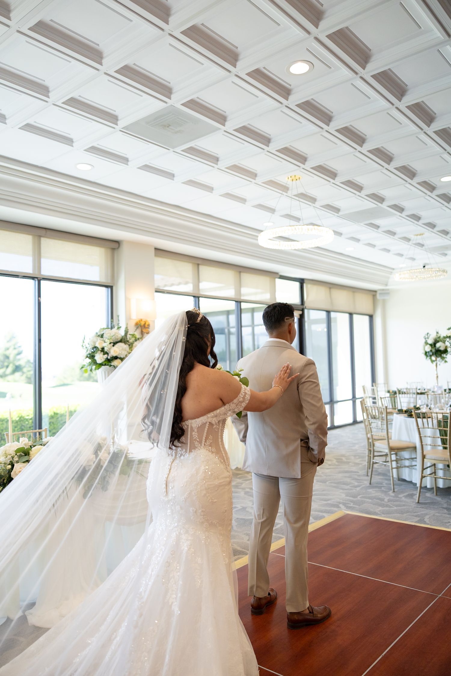 Bride and groom share first look moment in elegant ballroom with floral arrangements and gold chiavari chairs.