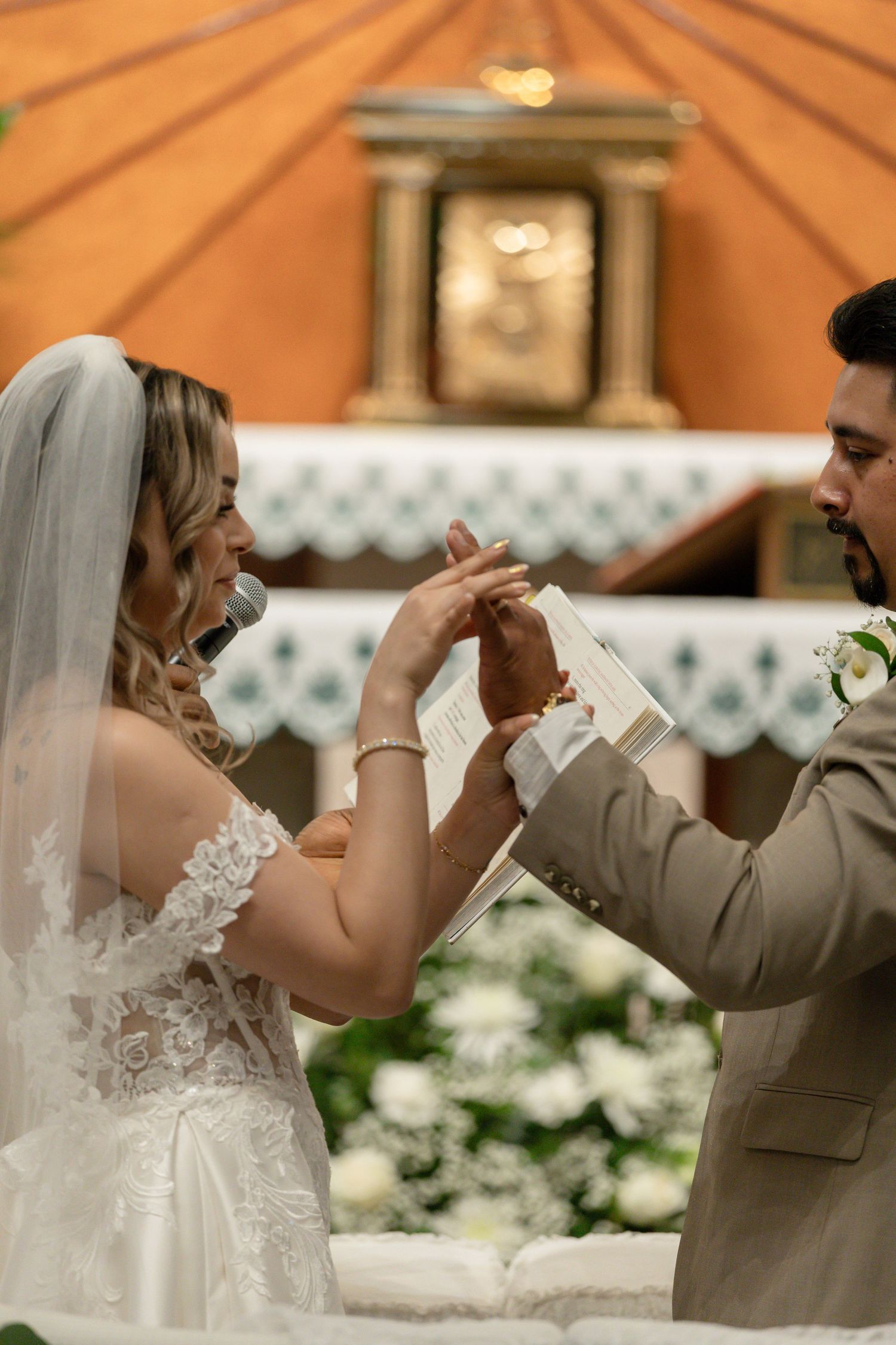 Bride and groom exchanging rings at church altar during wedding ceremony, bride in lace gown with veil.