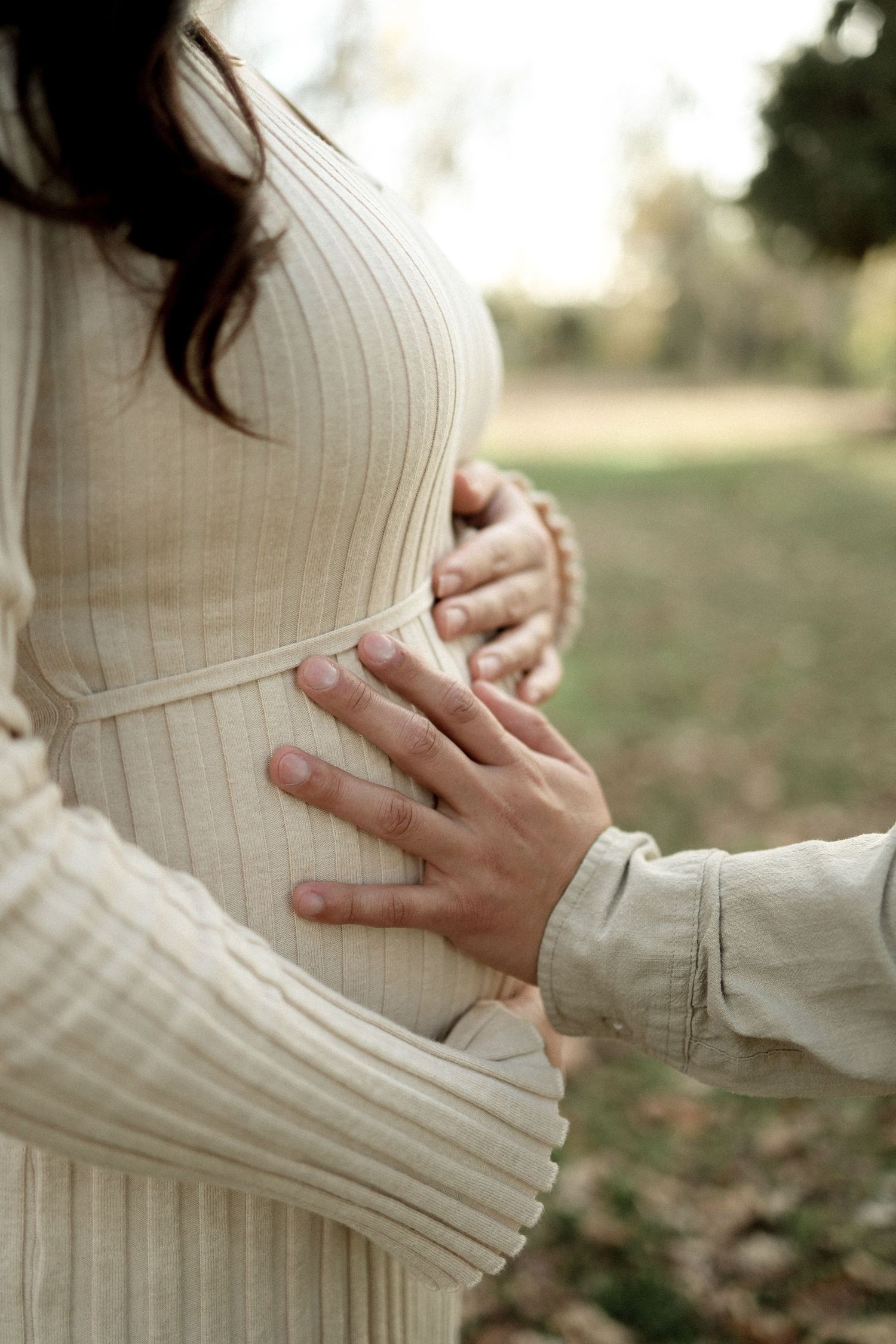 Close-up series of hands cradling a pregnant belly in a cream ribbed sweater against a soft outdoor background.