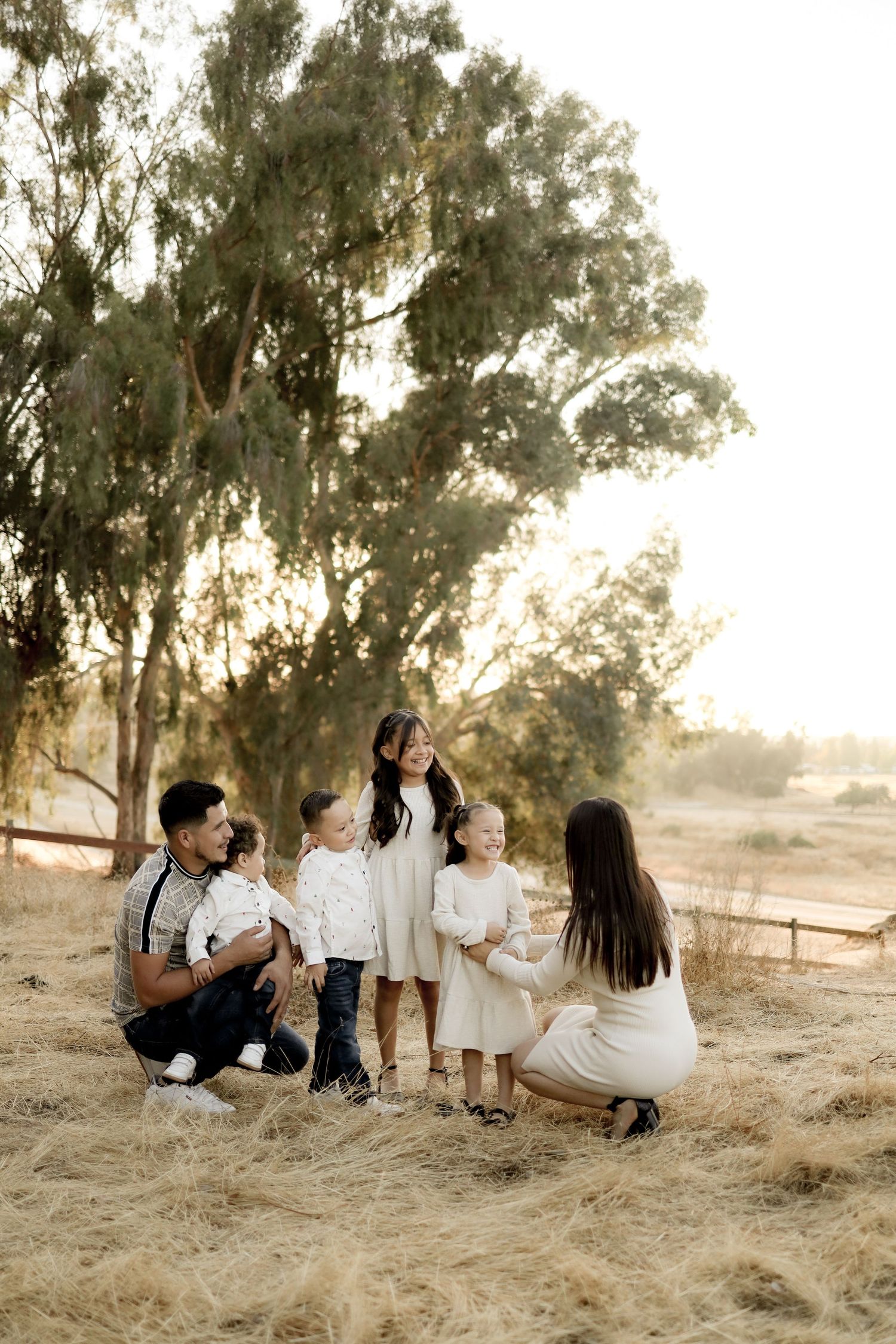 Family sitting together on dry grass in a natural outdoor setting during golden hour lighting.