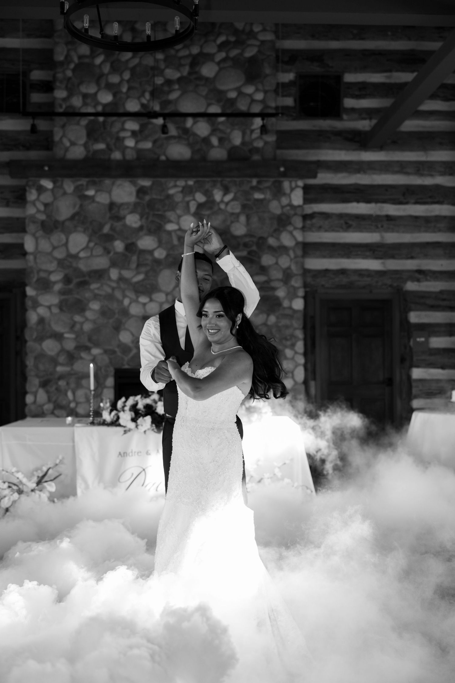 Bride and groom share first dance surrounded by dramatic fog machine clouds in rustic stone venue.