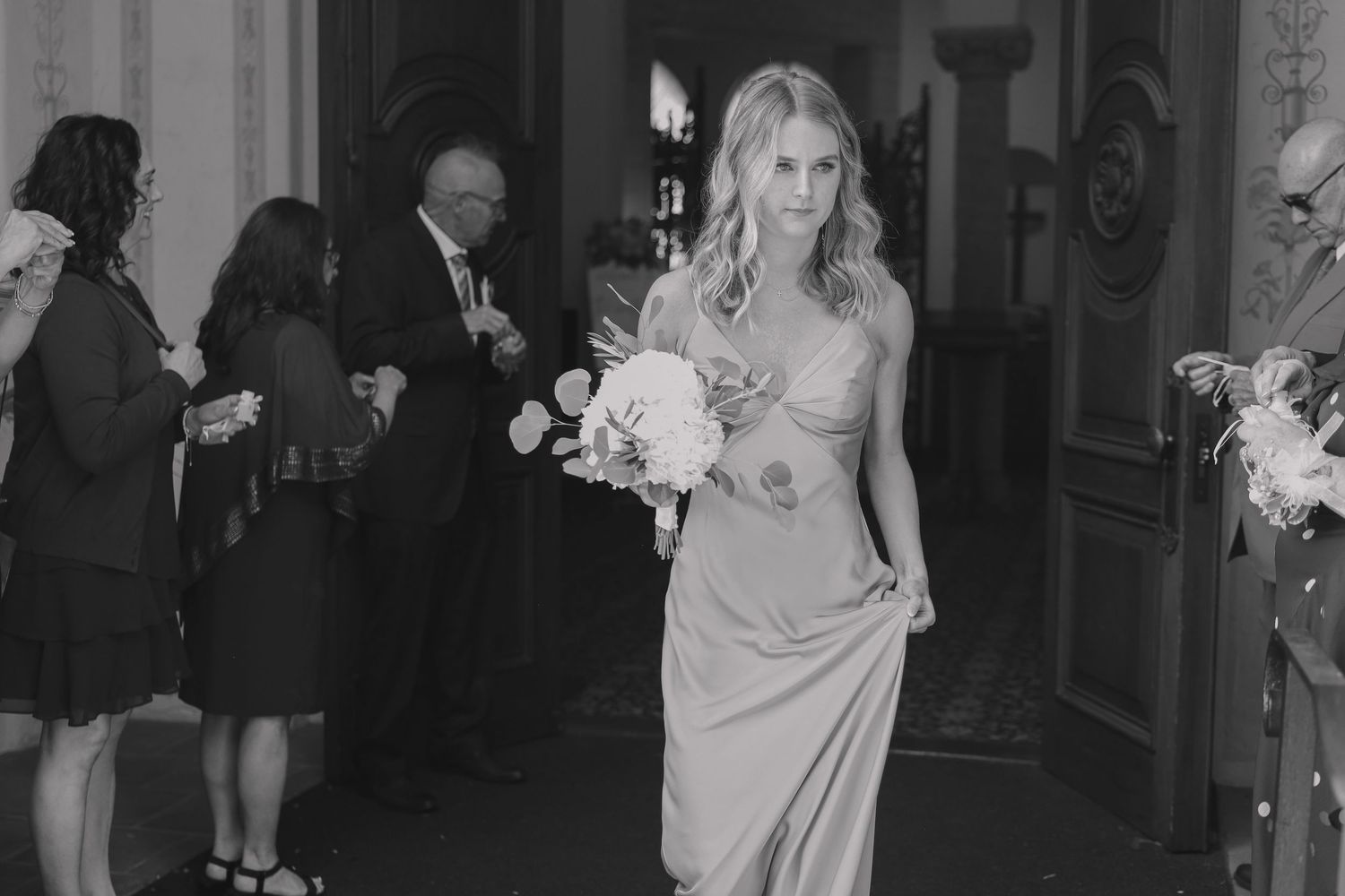 A group of people in formal attire dance and socialize at an elegant event in a black and white photograph.