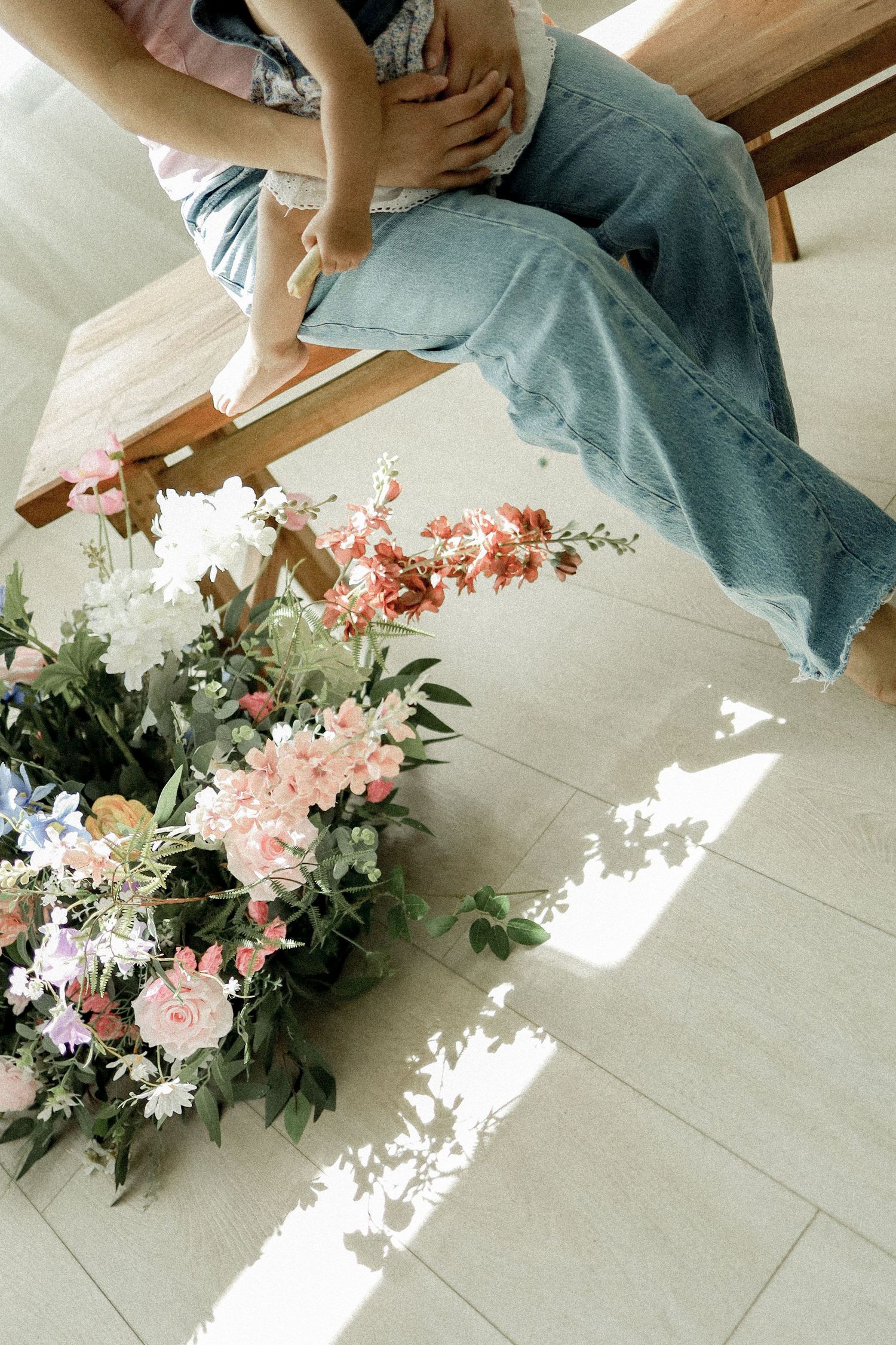 Pink floral arrangement with roses and greenery on white tile floor in sunlight.