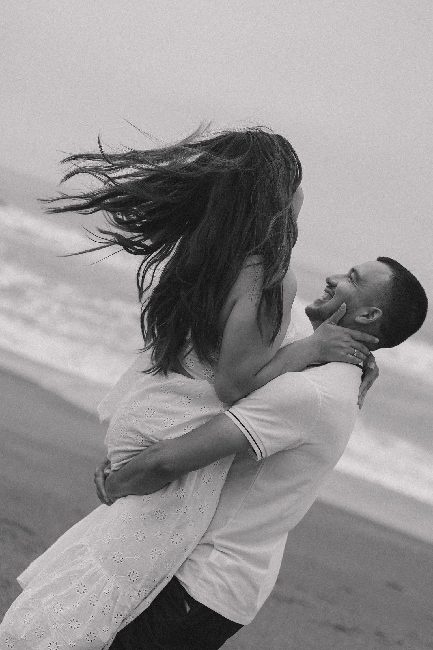 Romantic black and white photo sequence of an embrace on the beach with windswept hair.