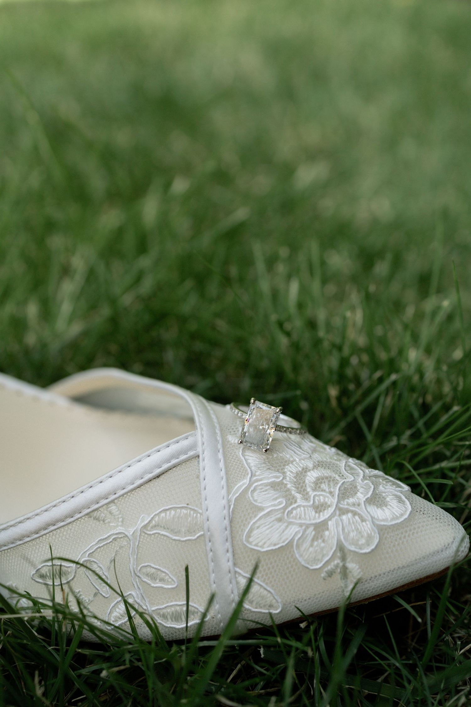 White embroidered bridal shoe with delicate butterfly details resting on grass.