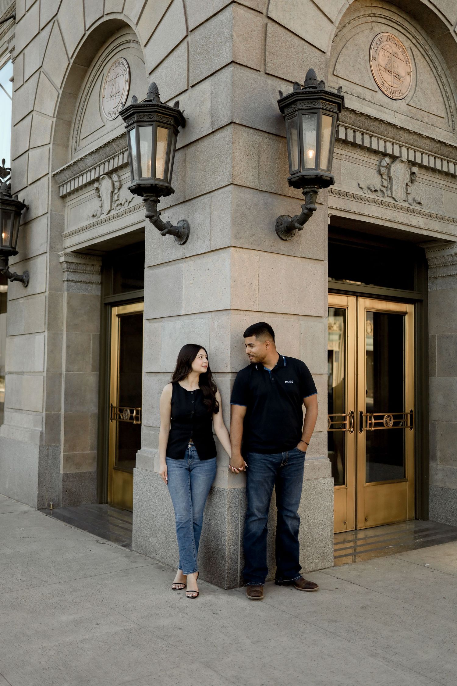 A couple shares intimate moments against a stone building exterior with arched doorways and wall sconces.