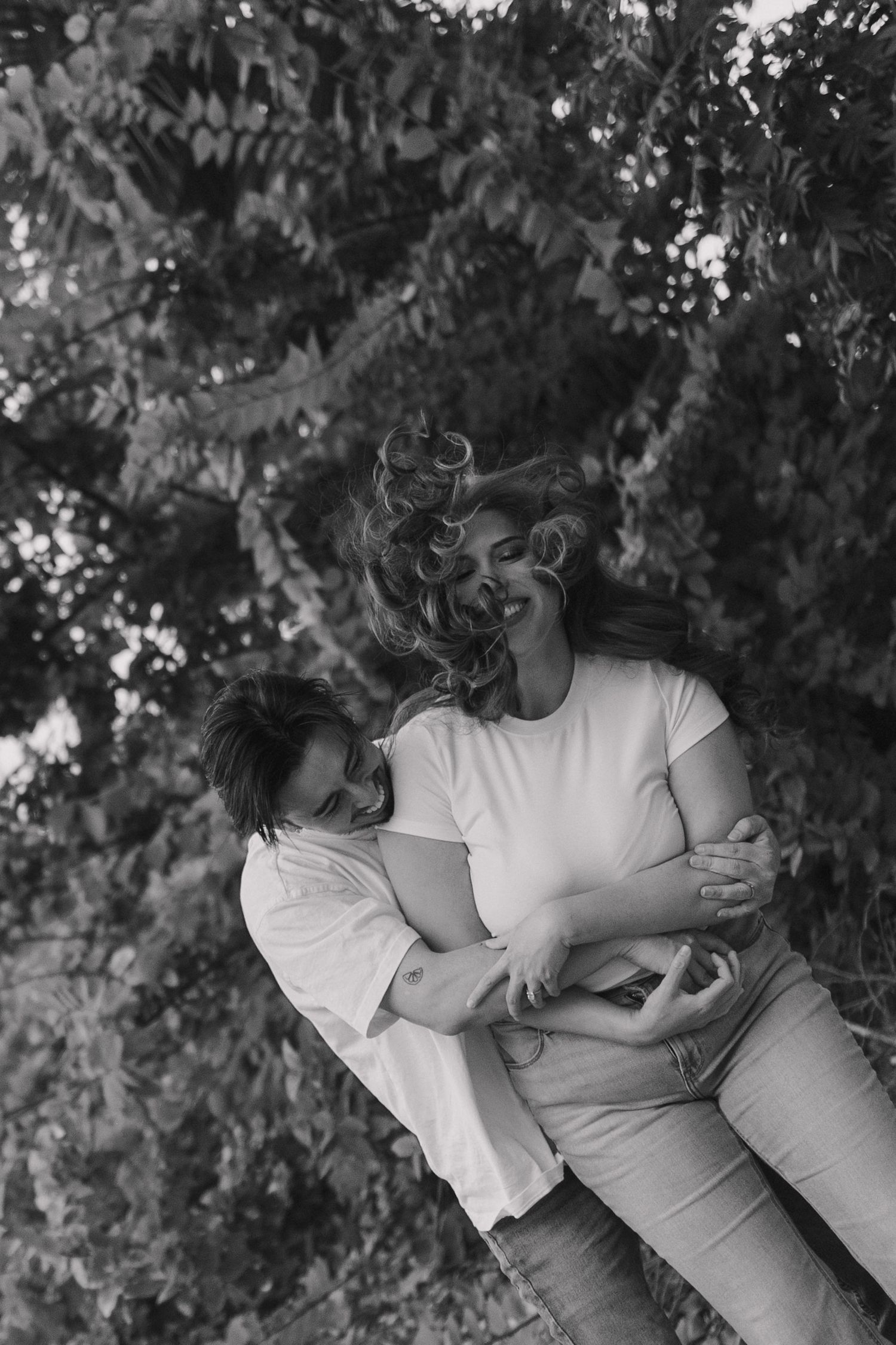Black and white photo series of a couple embracing intimately outdoors against a leafy background.