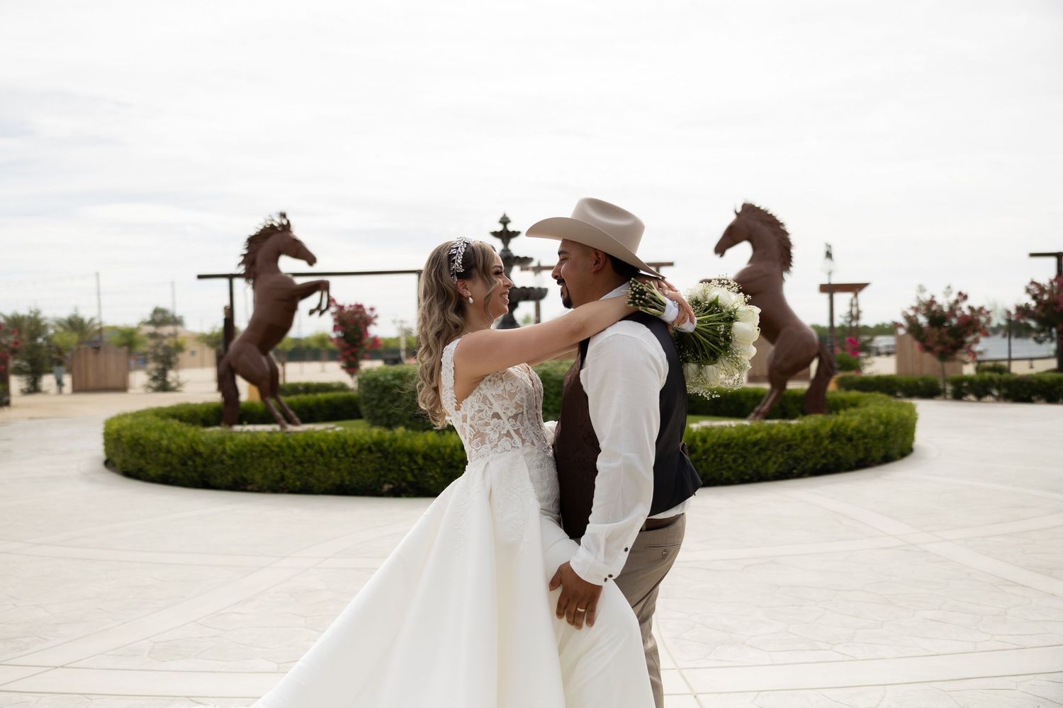 Bride and groom share a romantic dance outdoors near bronze horse sculptures at an elegant wedding venue.