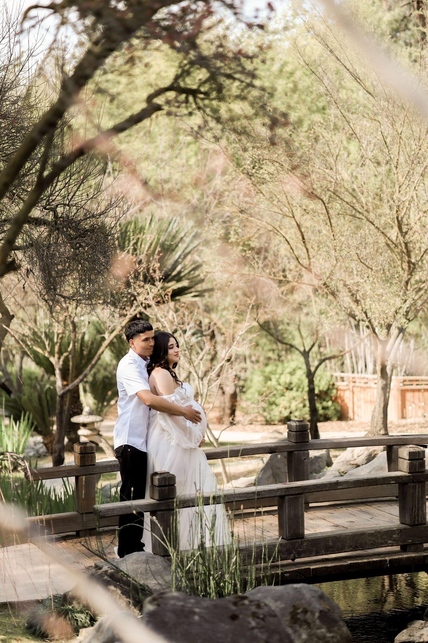A couple shares a romantic moment on a rustic wooden bridge surrounded by lush garden foliage.
