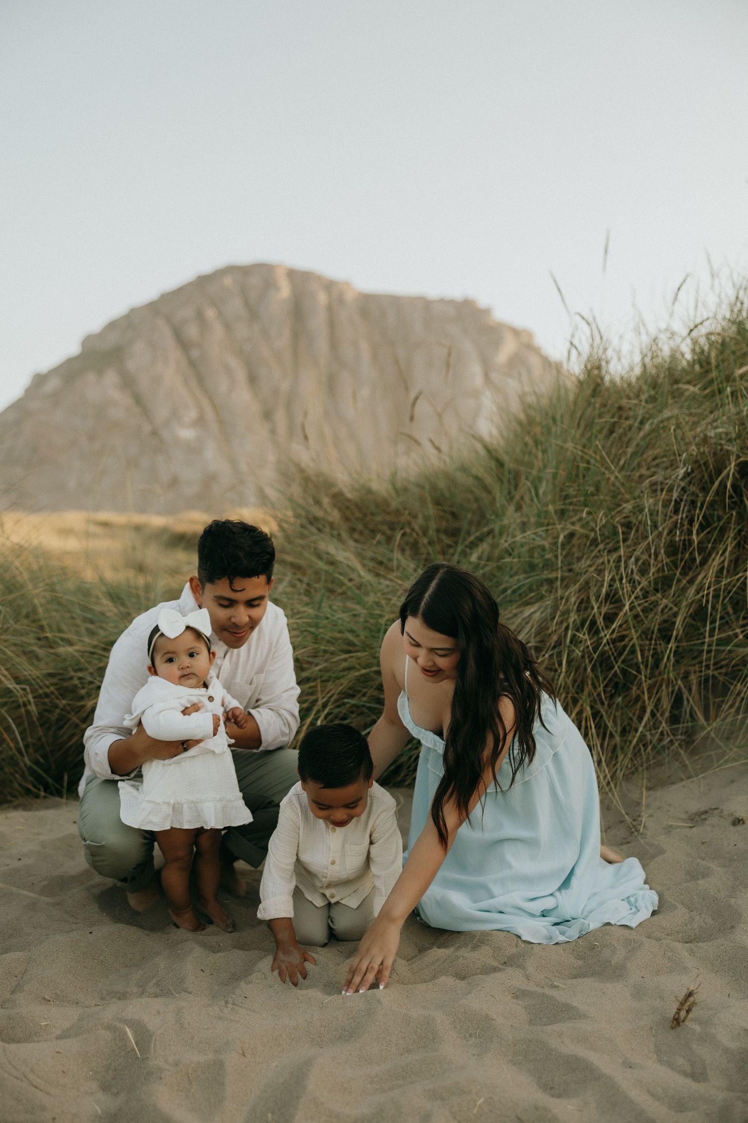 Family playing together on sandy beach dunes during golden hour.