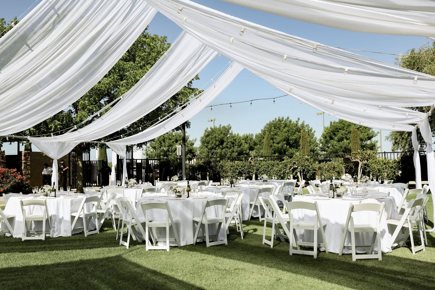 Elegant outdoor wedding reception setup with white draping and string lights.