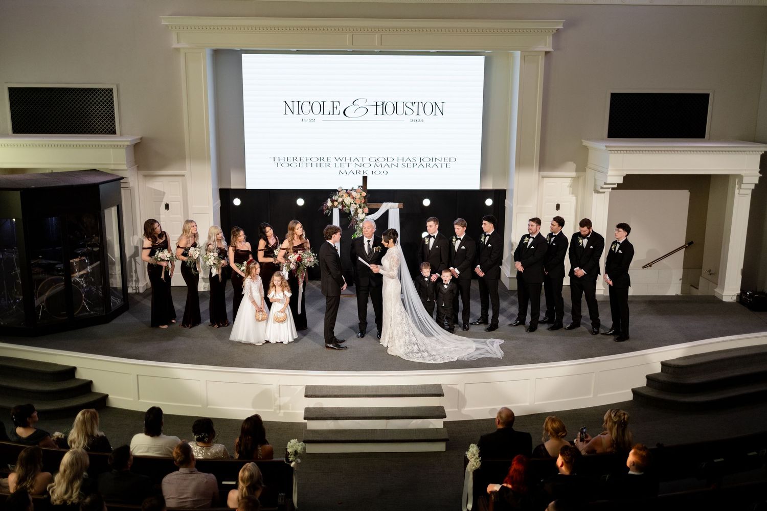 Nicole and Houston wedding ceremony with bridal party on church altar stage with projection screen backdrop.