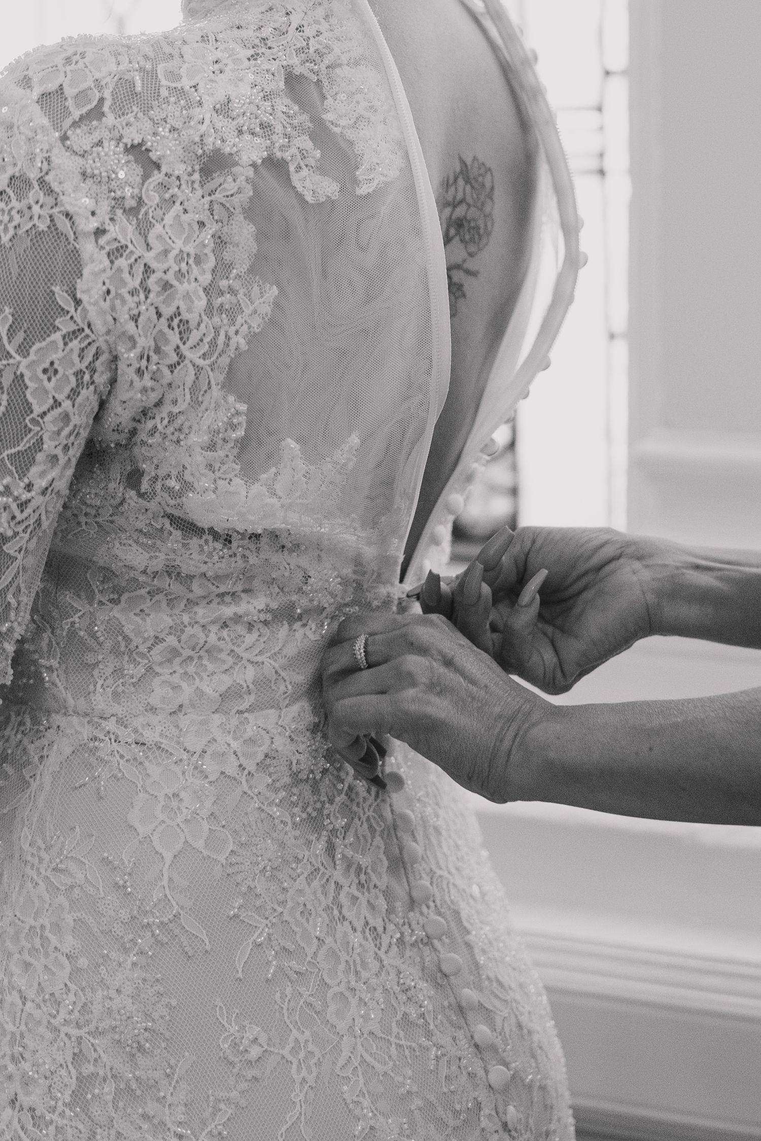 Black and white photo of hands fastening buttons on back of lace bridal gown.