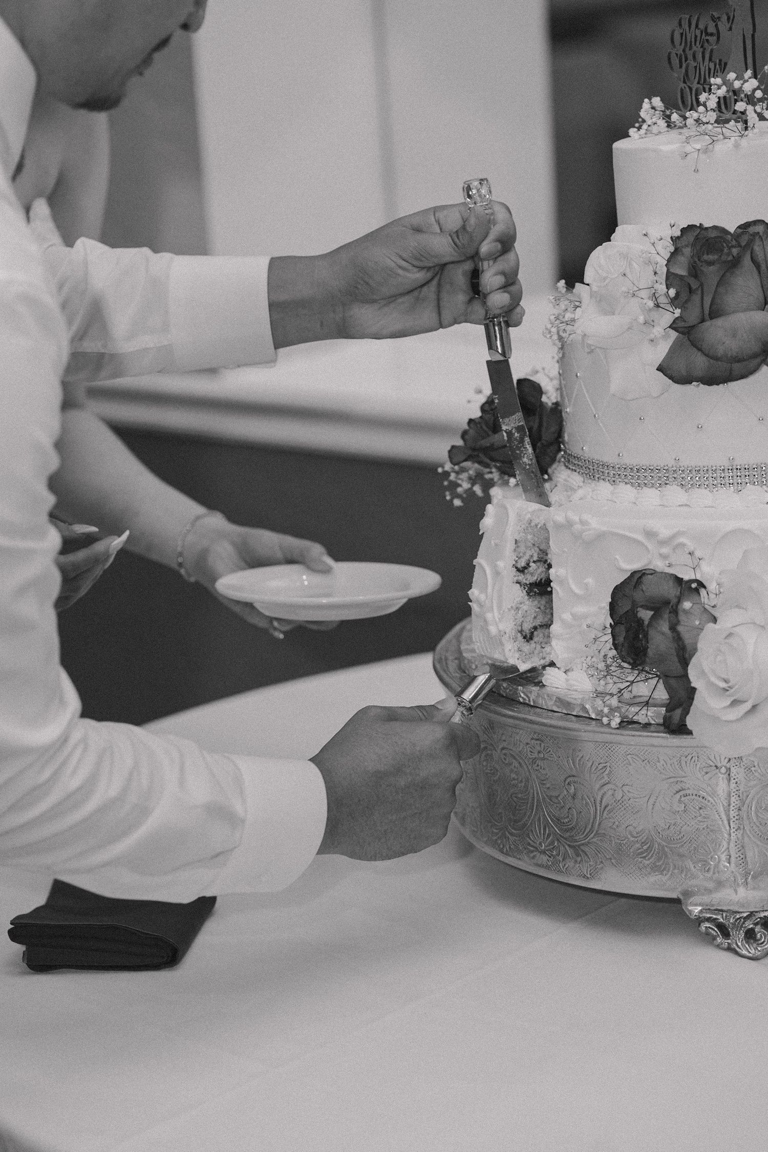 Black and white sequence showing the cutting of an ornate tiered wedding cake.