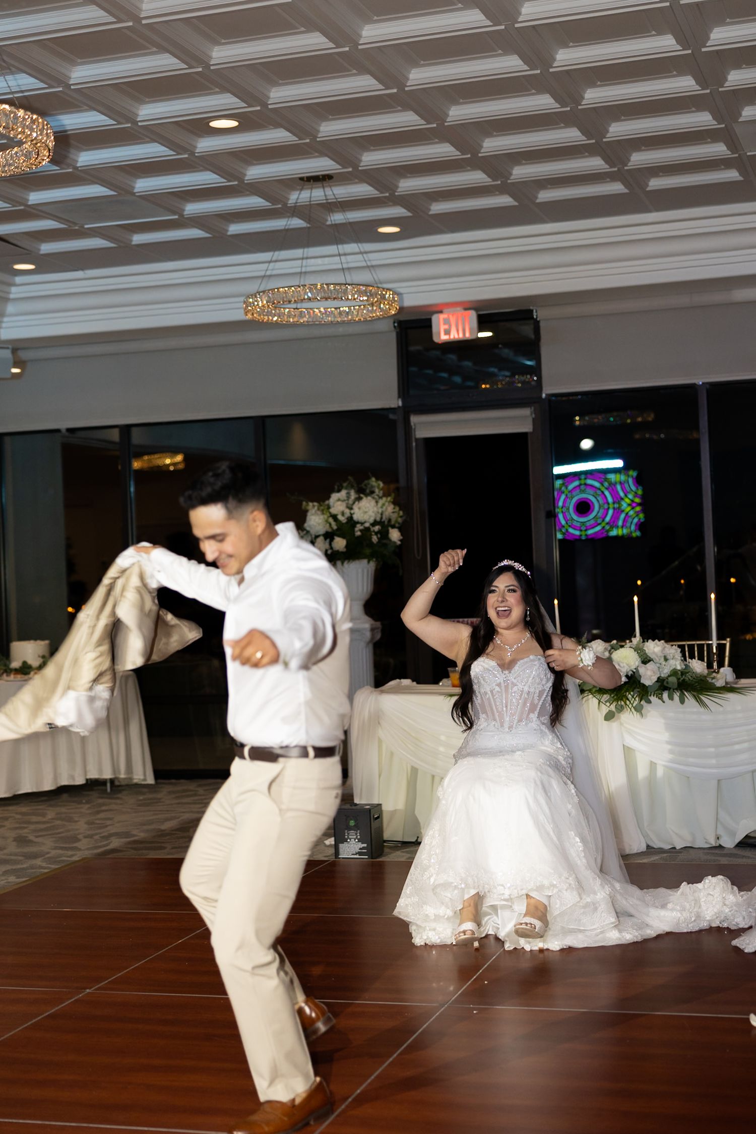 Bride and groom share a joyful first dance at their elegant wedding reception in a decorated ballroom.