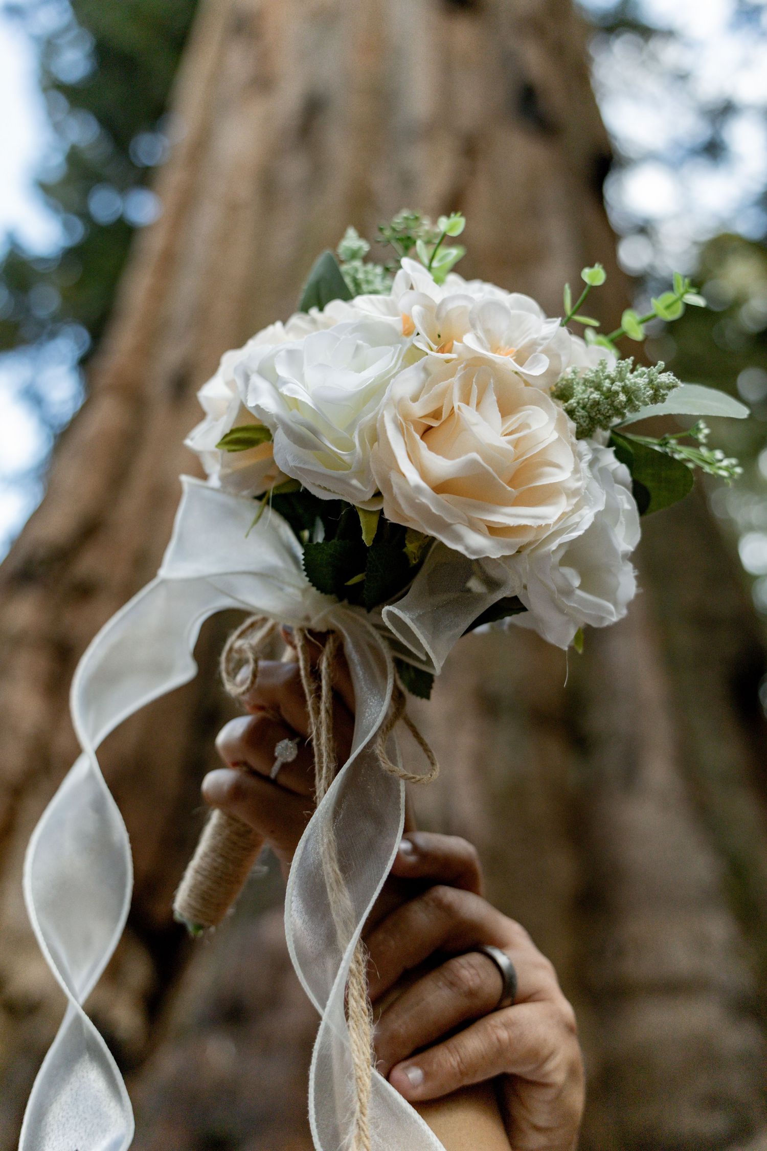 Delicate white rose wedding bouquets wrapped with ivory ribbons against a blurred natural background.