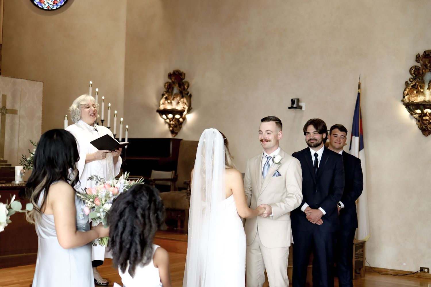 Wedding ceremony taking place in an elegant church with ornate lighting fixtures.