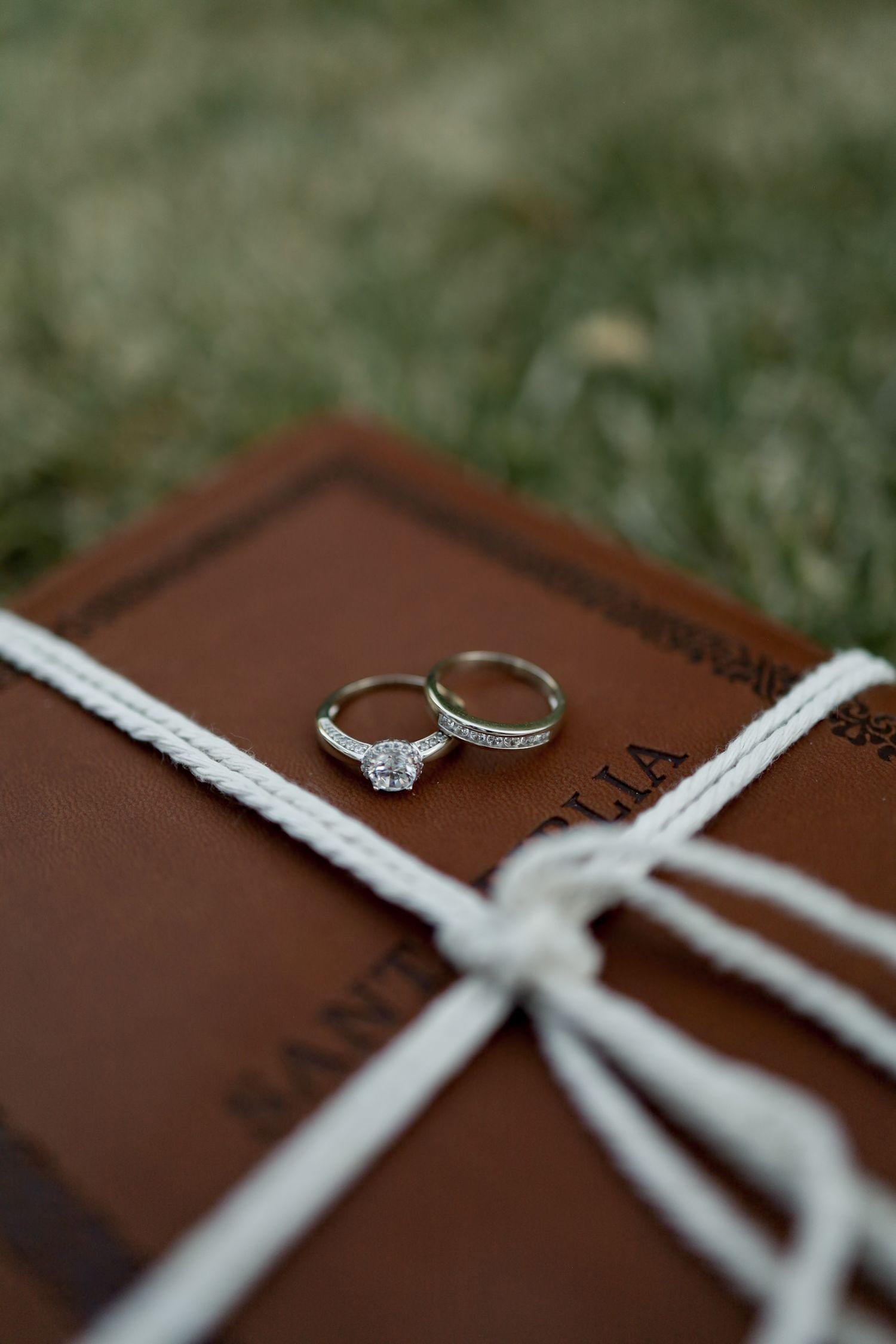 Wedding rings displayed on brown leather with white ribbon detail.
