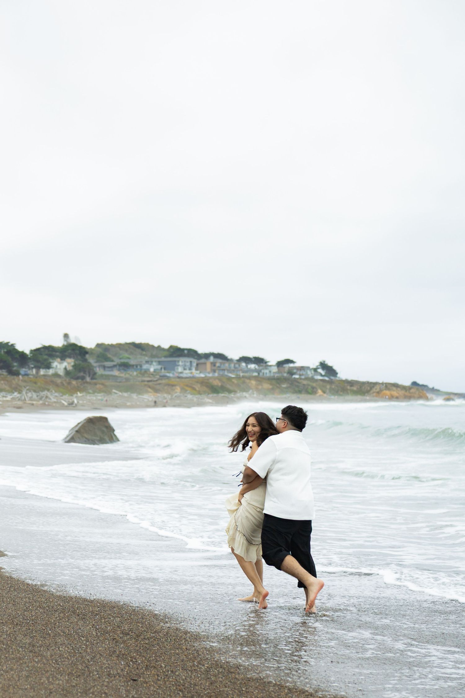 Couple playfully running and splashing in the ocean waves along a scenic beach coastline.