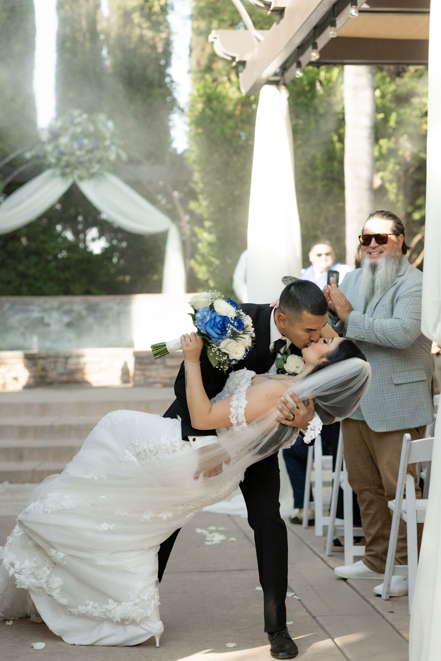Wedding party performs synchronized dance moves in formal attire under covered venue.