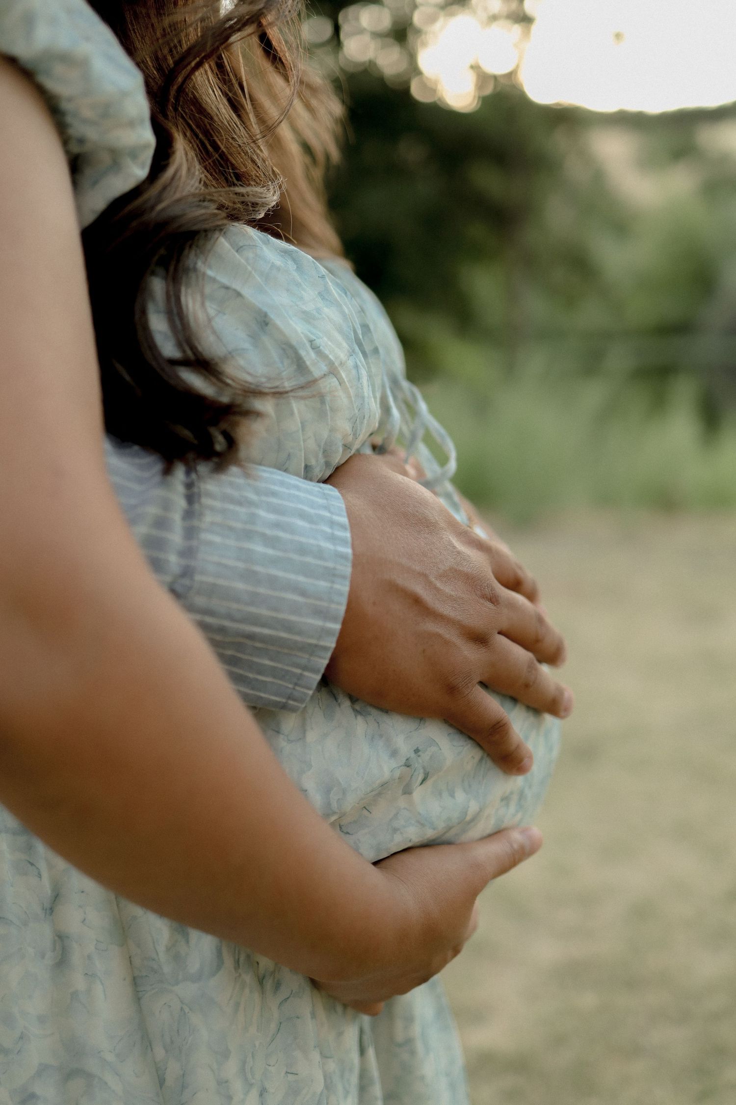 Close-up shots of hands gently cradling a pregnant belly in a striped dress.
