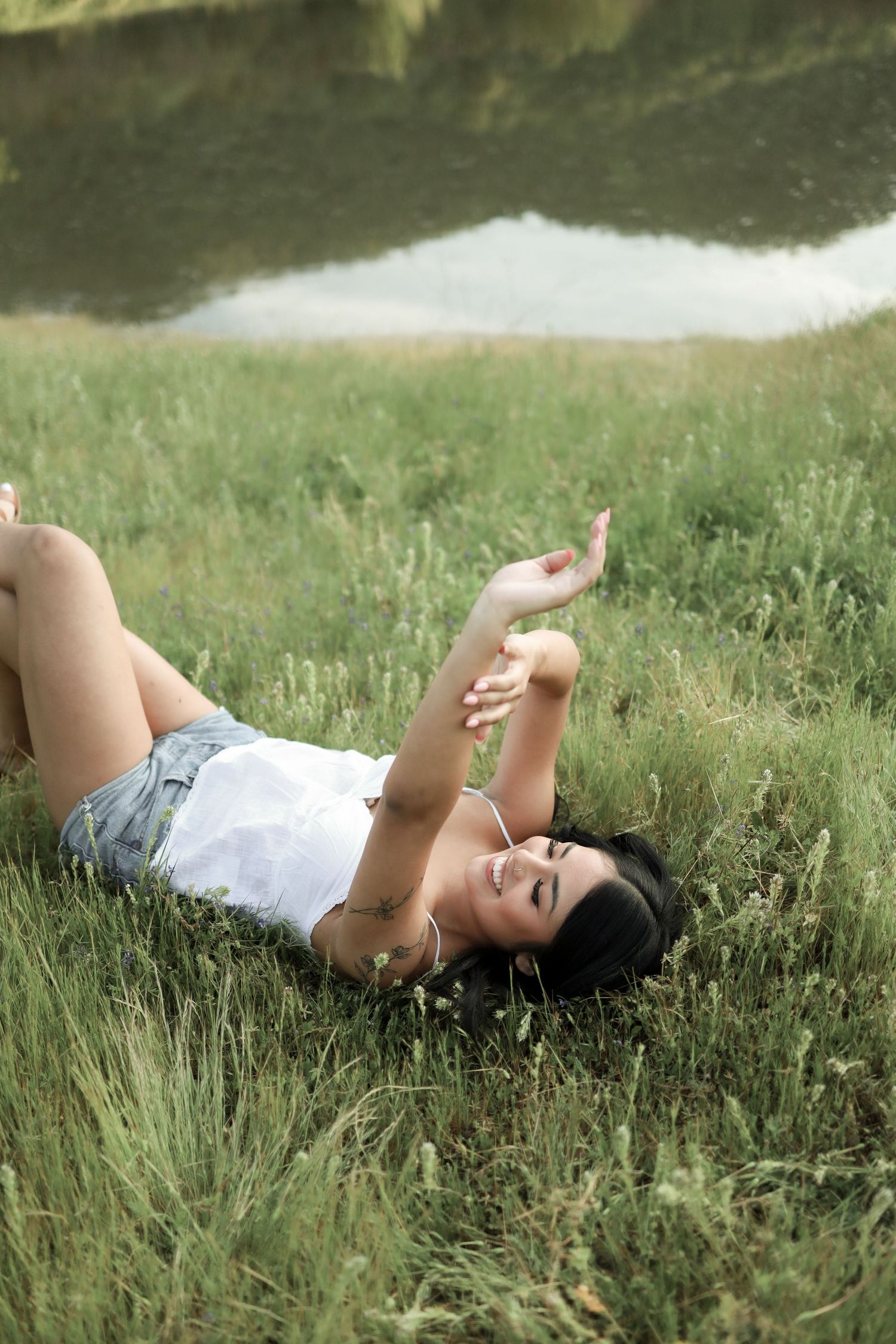 Serene shots of someone relaxing in white clothing on green grass by the water.