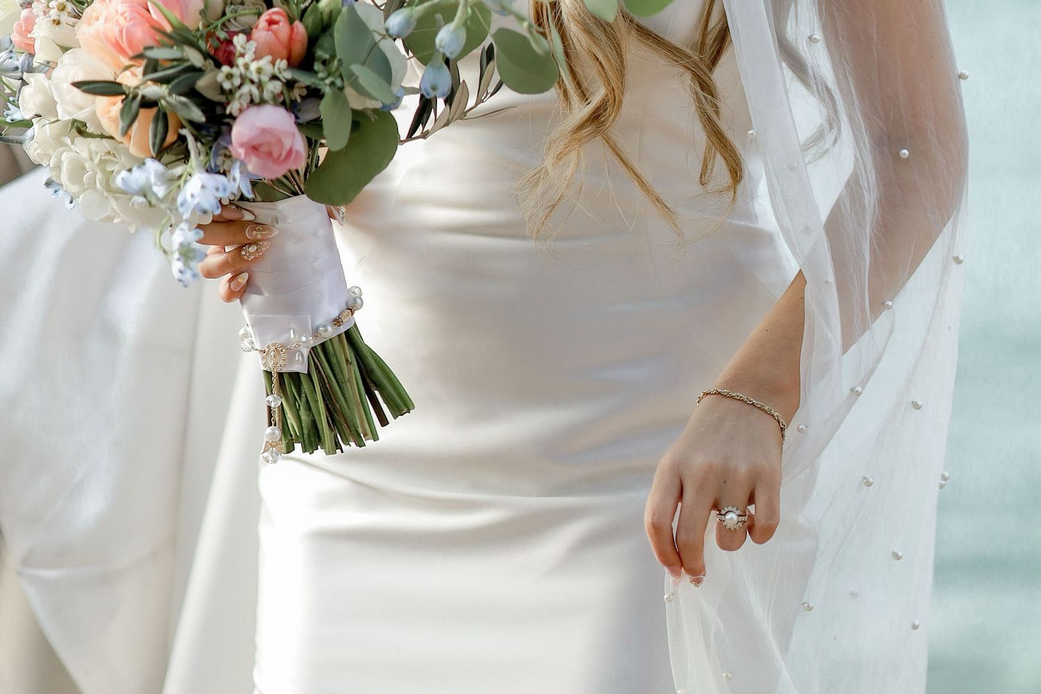 Close-up of bride holding romantic bouquet with pink roses and white flowers.