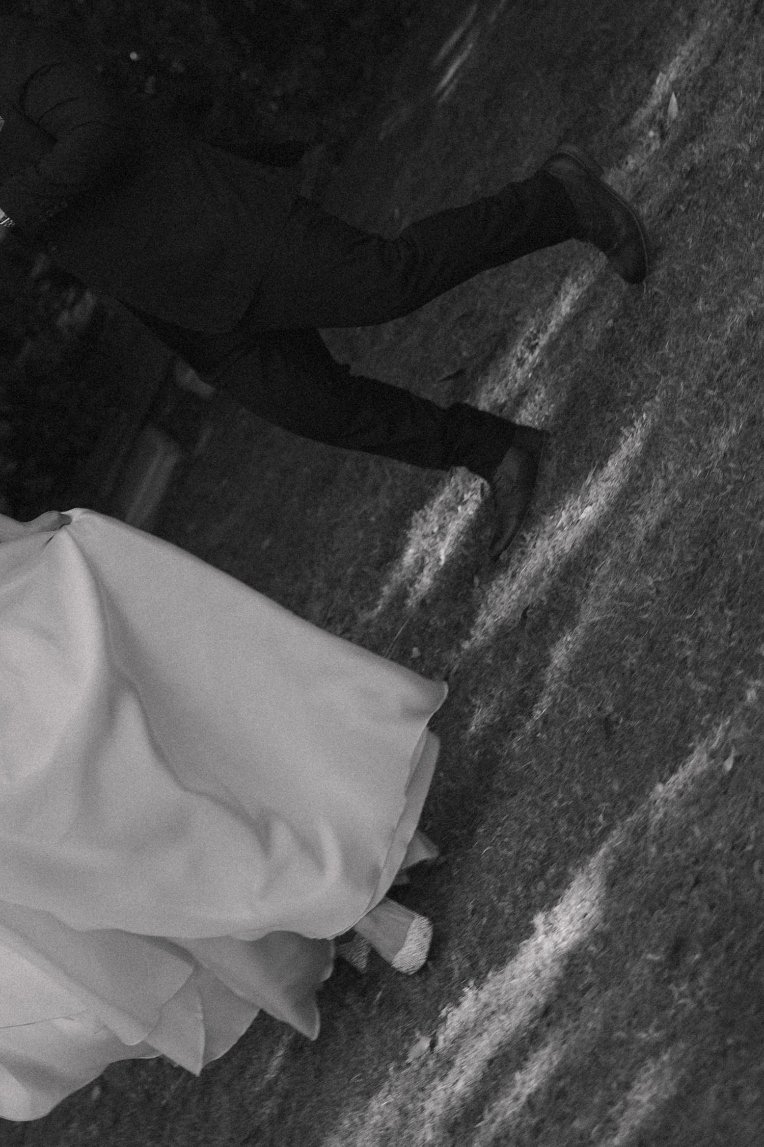 Black and white photo of a bride in white gown and groom in dark suit walking on pavement.