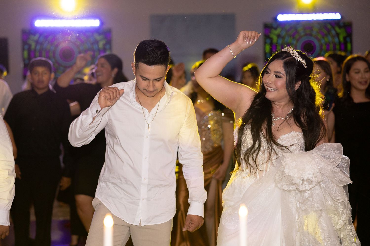 Bride and groom dancing joyfully at their wedding reception surrounded by guests in elegant attire.
