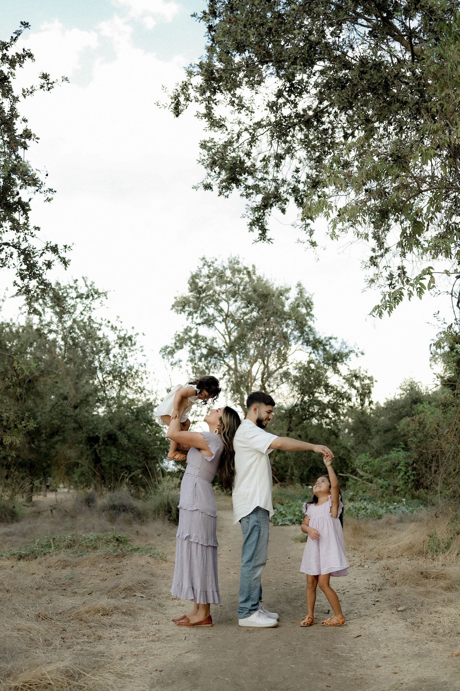 Three people in casual attire dance and pose playfully together in a natural outdoor setting with trees in the background.
