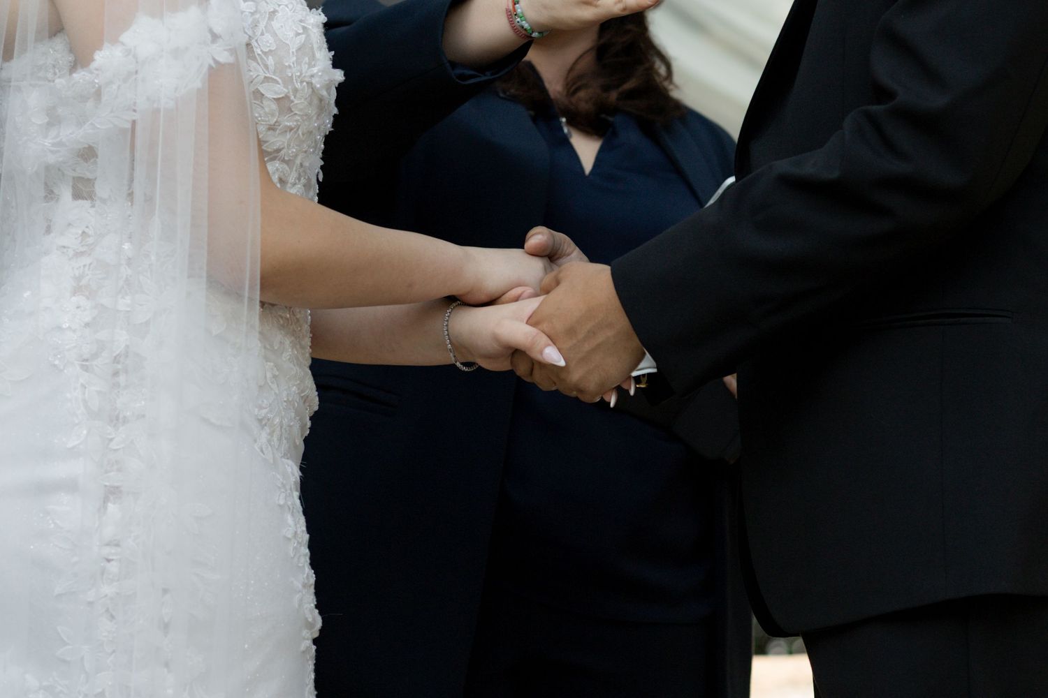 Close-up view of hands exchanging rings during a wedding ceremony with white lace dress details visible.