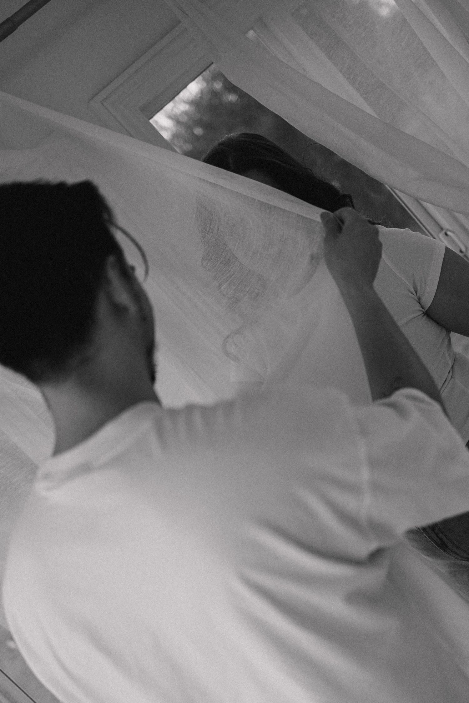 A person adjusting white fabric or veil in black and white photography.
