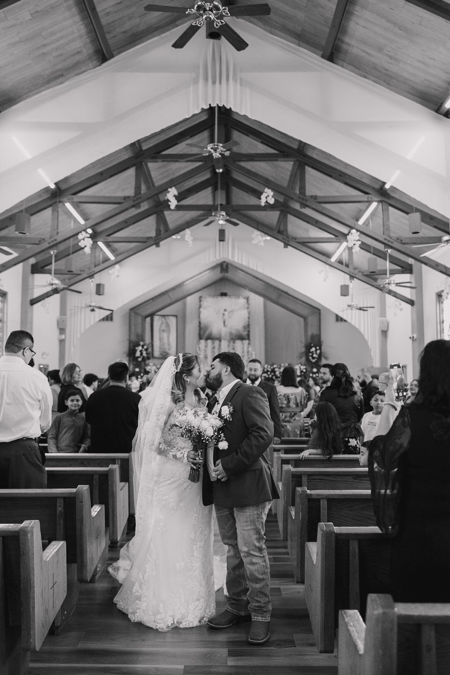 Black and white photo of a bride and groom sharing a kiss at the altar of a rustic wooden church.