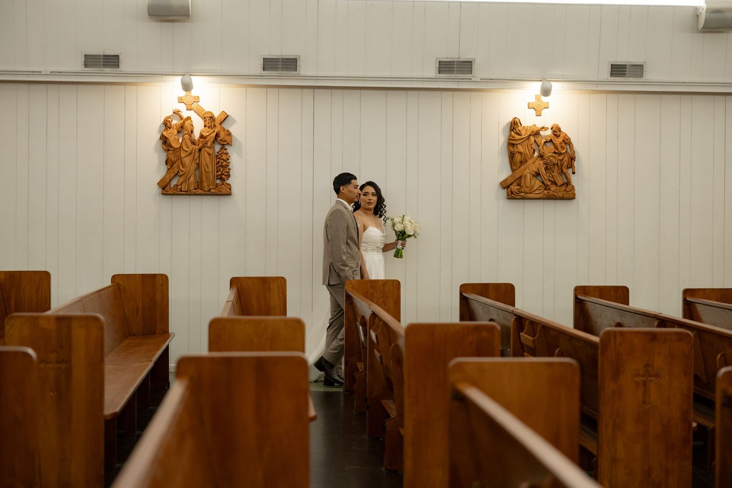 Couple embracing in church aisle surrounded by wooden pews on their wedding day.