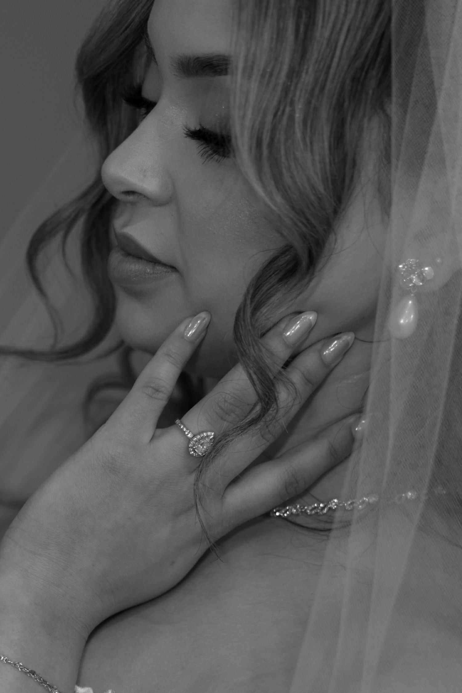 Black and white bridal portrait showing bride with veil, diamond ring, and manicured nails touching her face.