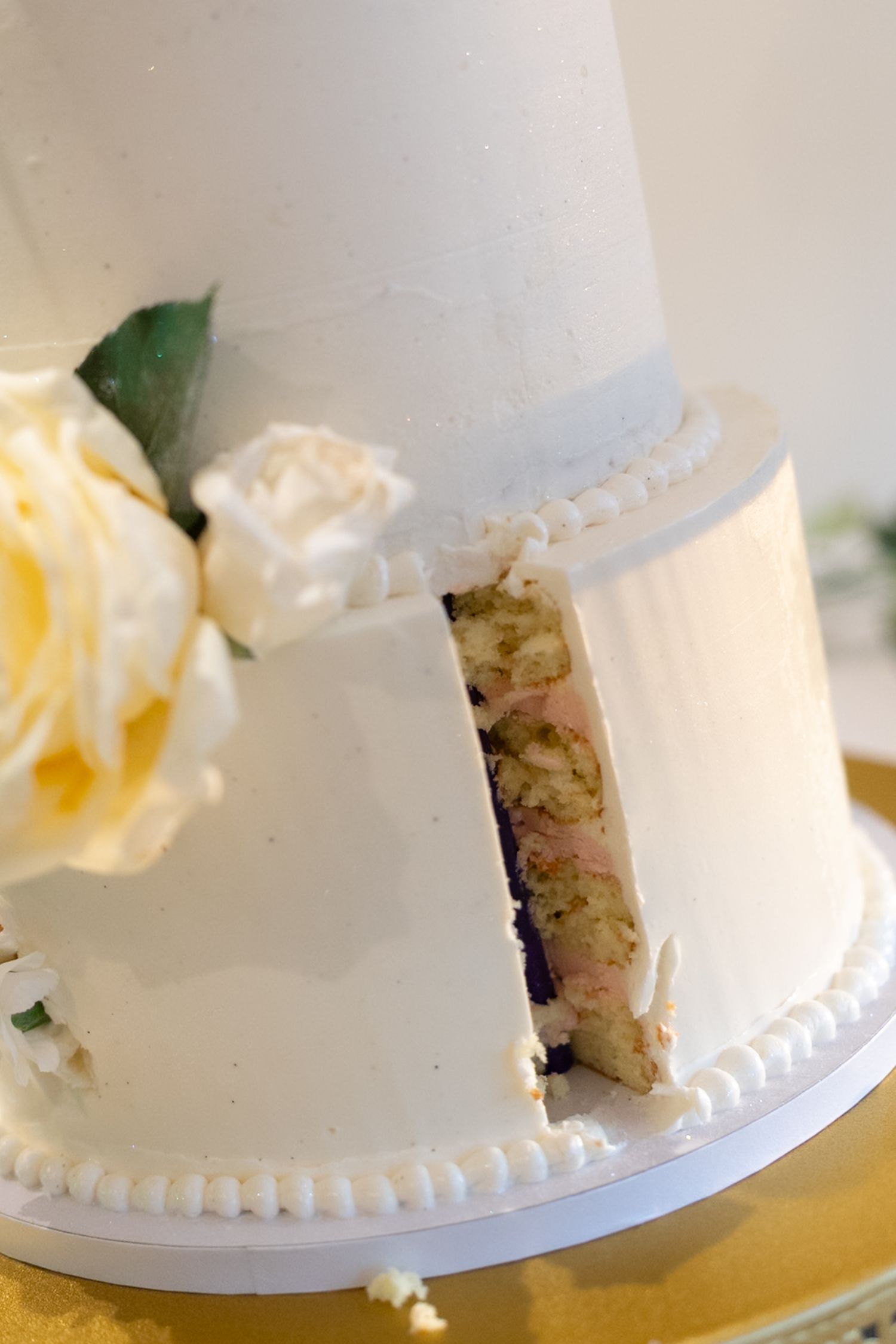 Sliced two-tier white wedding cake with floral decorations revealing colorful layers inside.