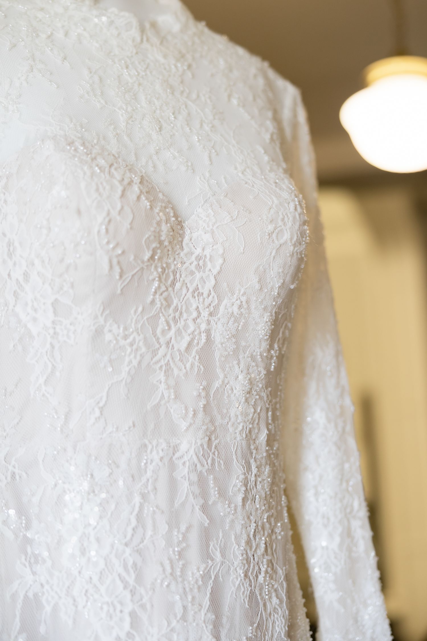 Close-up of a long-sleeve lace wedding dress with intricate floral beading on a hanger.