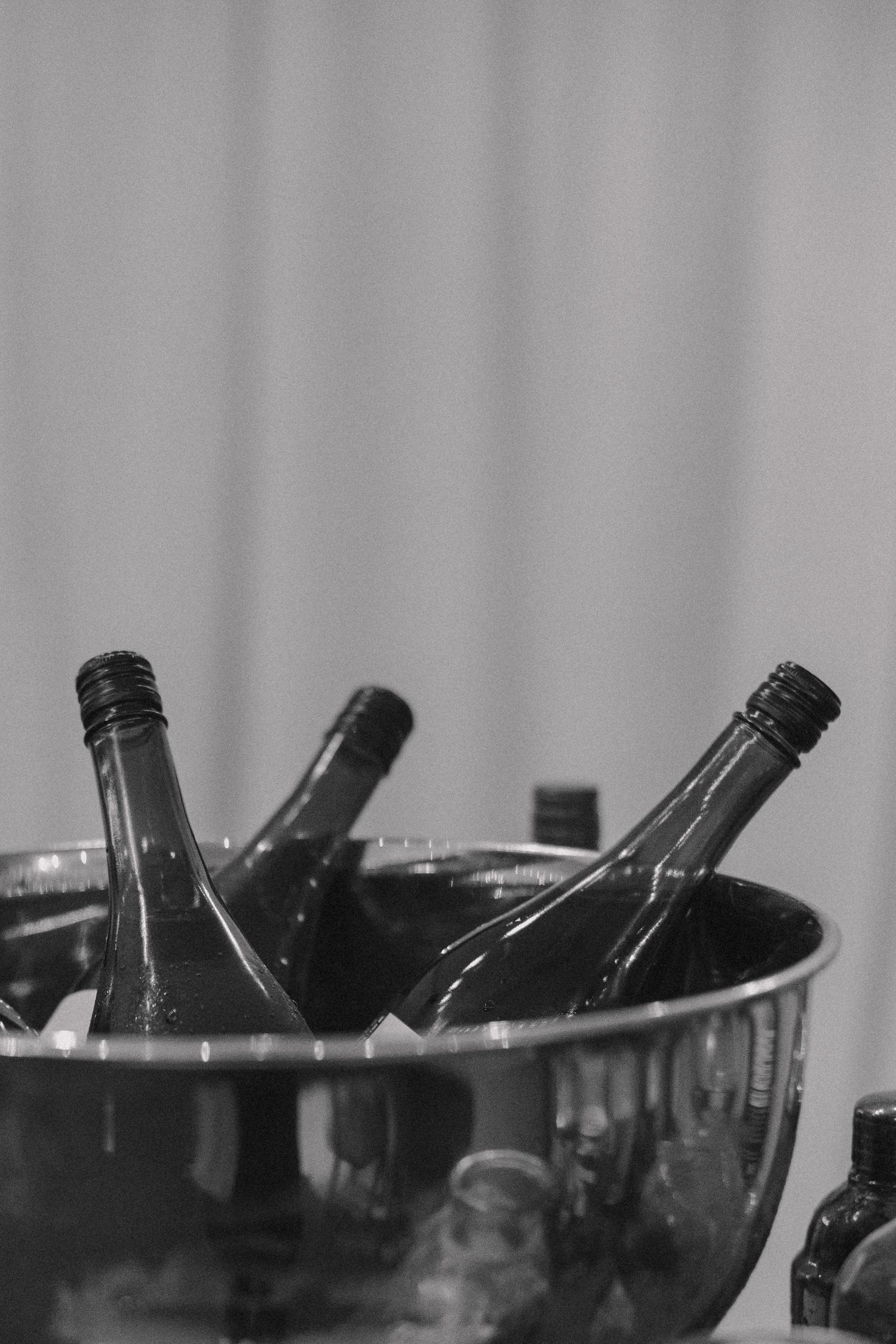 Black and white photo of champagne bottles chilling in silver ice bucket at wedding reception.