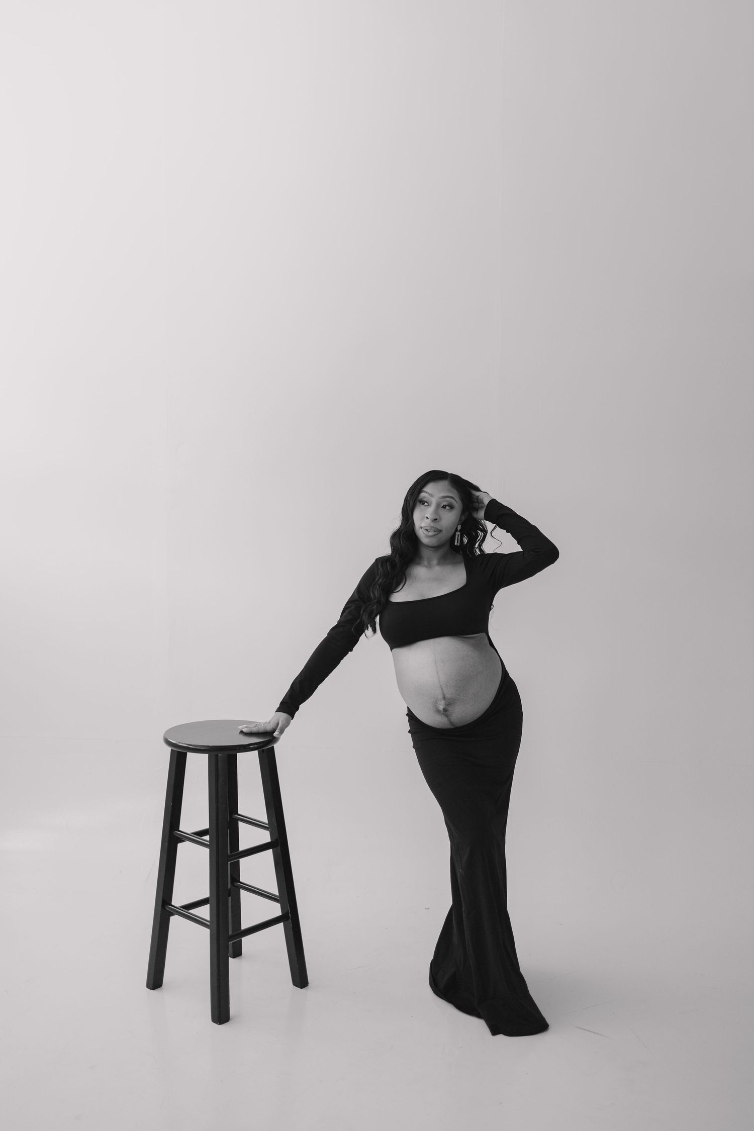 Dramatic maternity portraits in black and white featuring elegant poses with wooden stool.