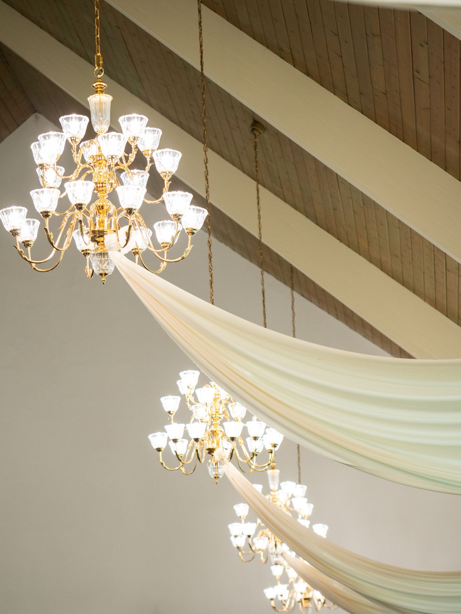 Elegant crystal chandeliers with white fabric draping create a romantic wedding venue ceiling.