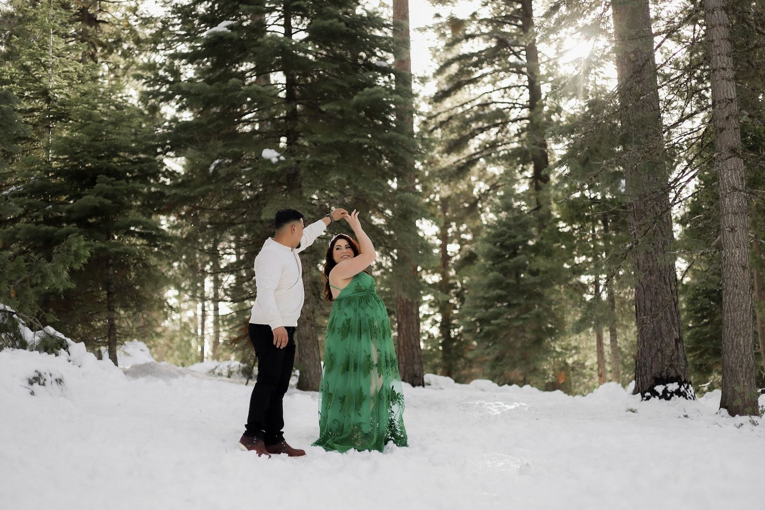 Winter pregnancy announcement photoshoot in a snow-covered pine forest.