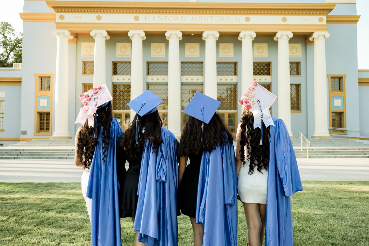 Graduates in blue caps and gowns pose for photos in front of a grand columned building on graduation day.