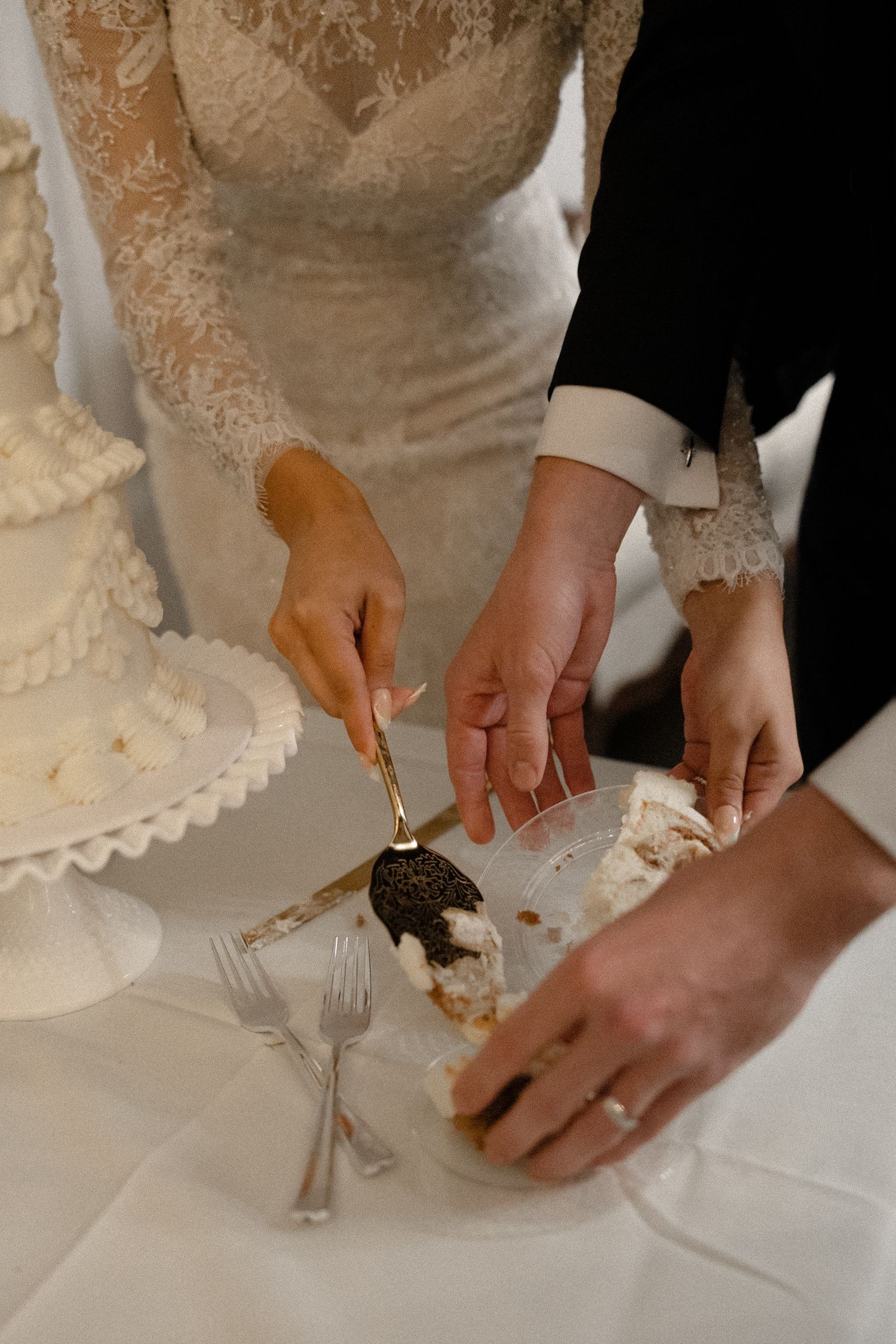 Bride and groom cut white wedding cake together, placing slice on plate at reception.