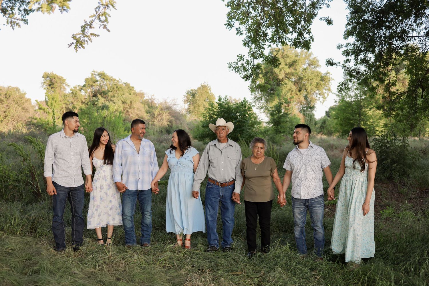 A group of people in casual attire standing together outdoors in a natural setting with trees and greenery in the background.