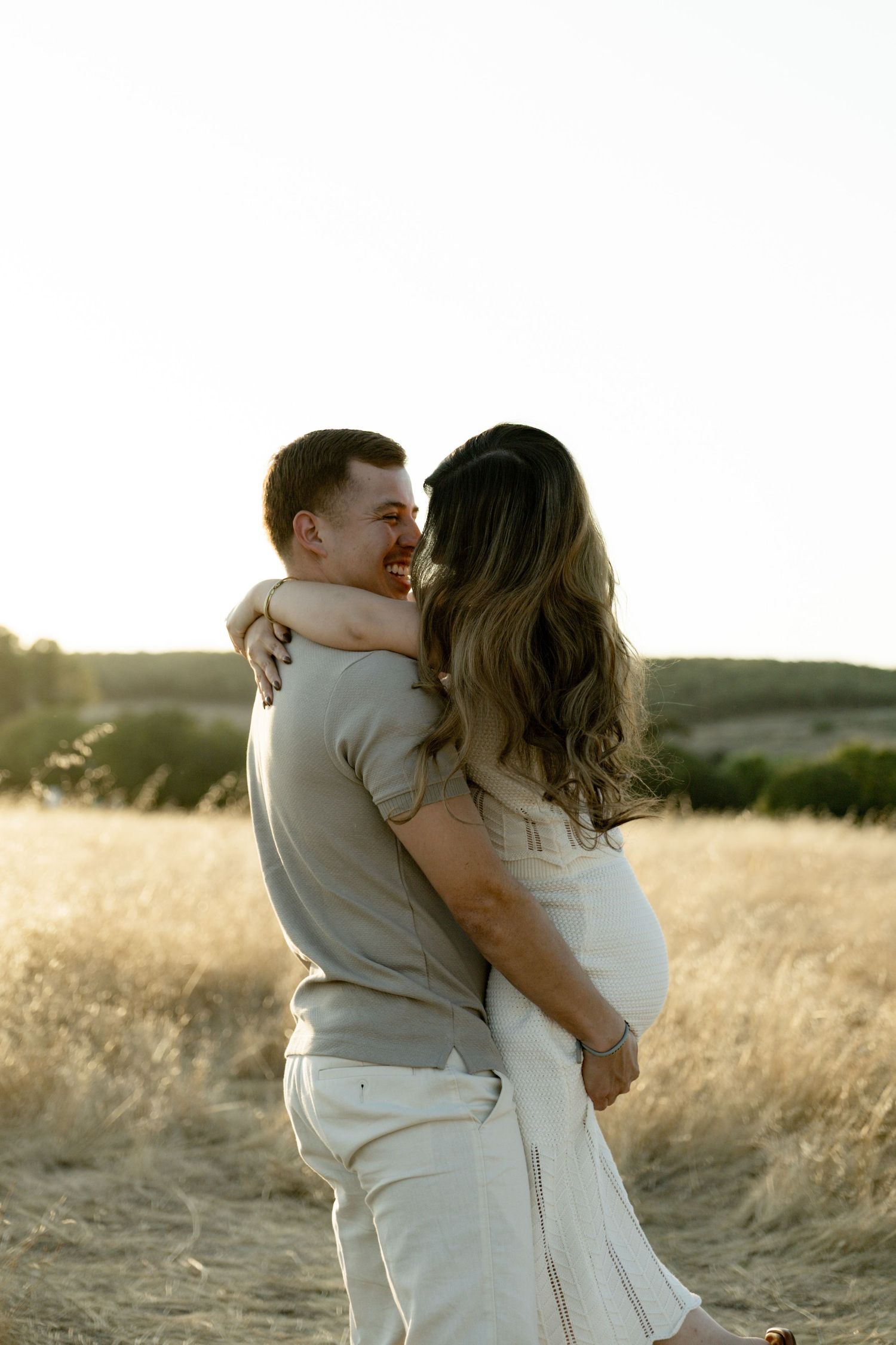 Couple embracing in a sunlit field of tall grass during sunset.