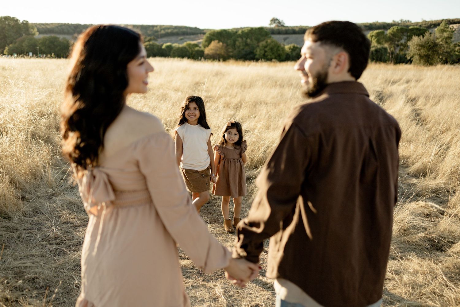 Family strolling through tall grass in a sun-drenched field during golden hour.